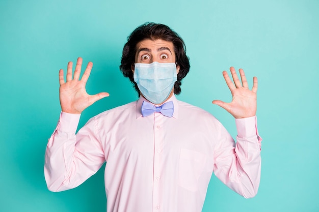 Photo of frightened man dressed pink shirt medical mask two arms up isolated turquoise color background