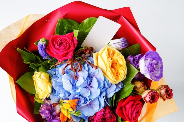 Photo from above bouquet of multi-colored roses with card on empty white background