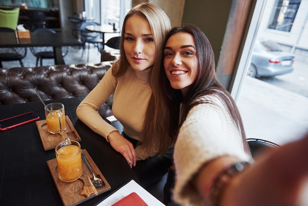 Фото с телефона девушки. Молодые подруги принимают селфи в ресторане с двумя желтыми напитками на столе