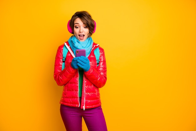 Photo of funny blogger lady look telephone screen read positive\
comments likes wear casual red coat blue scarf gloves ear covers\
pants