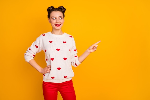 Photo of funny cheerful lady show sale low prices indicate finger empty space new banner advertisement wear hearts pattern white sweater