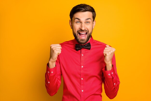 Photo of funny macho guy good mood open mouth celebrating lottery money winning raise fists excited wear stylish red shirt with black bow tie 