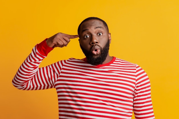 Photo of funny shocked man finger temple stupid grimace on yellow background