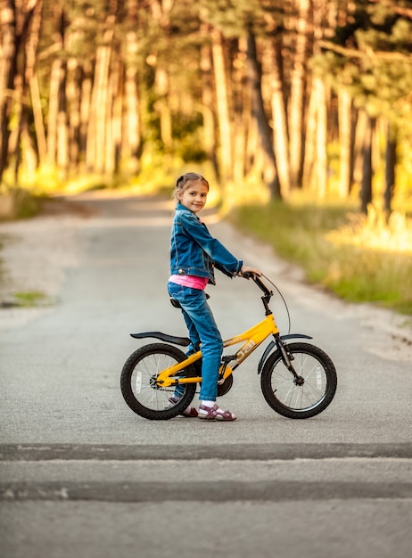 Foto di una ragazza in sella a una bici gialla nella foresta