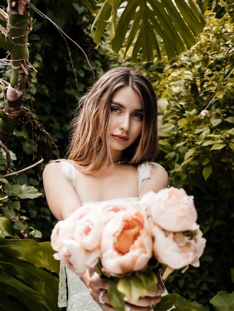 Photo of a girl wearing a dress and holding peonies in a greenhouse. selective focus