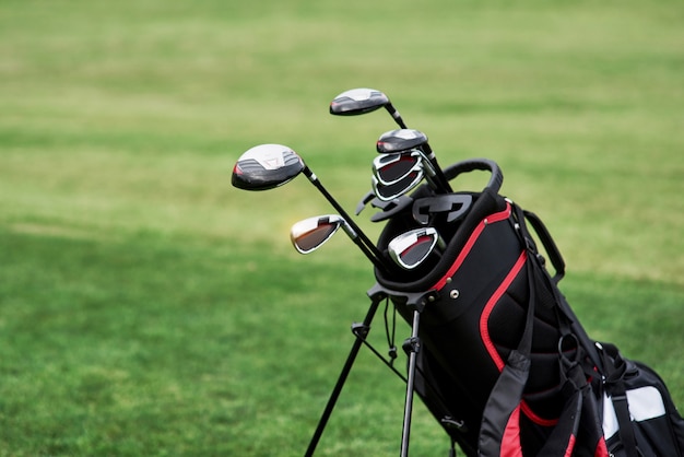 Photo of golf bag with sticks standing on the green lawn. Close up view.