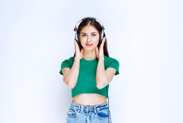 Photo photo of a good-looking girl model standing with headphones and posing against white wall.