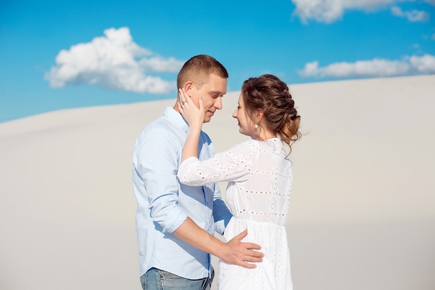 Photo of a gorgeous couple man and woman smiling and hugging on a sandy hill