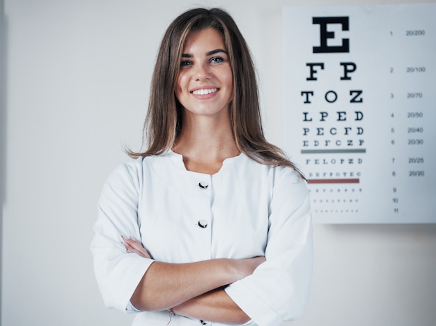 Photo of gorgeous female ophthalmologist posing over board with letters.