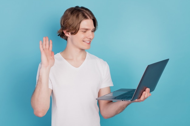 노트북을 들고 있는 남자의 사진은 안녕하세요 손 화상 통화를 하는 흰색 티셔츠를 입고 파란색 배경에 격리되어 있습니다.