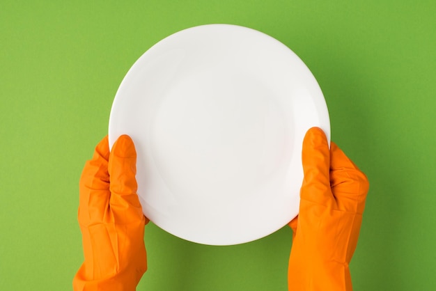 Above photo of hands in orange gloves holding a plate isolated on the green background