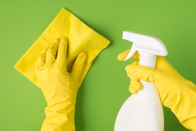 Sopra la foto delle mani in guanti gialli che tengono spray detergente e straccio per la pulizia isolati su sfondo verde