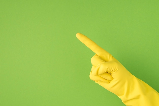 Above photo of hands in yellow gloves making the gesture as directing with index finger isolated on the green background