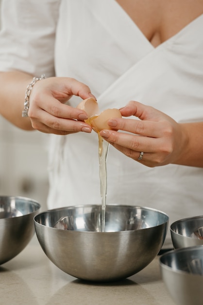 Una foto delle mani di una giovane donna che sta separando il tuorlo dall'albume sopra la ciotola di acciaio inossidabile in una cucina.