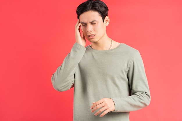 A photo of a handsome Asian man rubbing his head with his hand because of his migraine