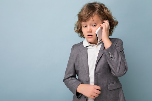 Photo of Handsome boy with curly hair wearing grey suit holding and using phone