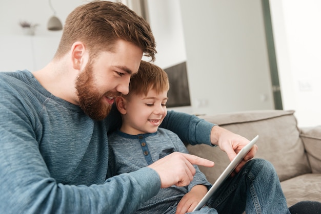 彼の小さなかわいい息子とタブレットコンピュータを使用してハンサムな父の写真。