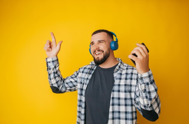 Photo of a handsome guy listening to youth music in his ears dancing a young man in a plaid shirt and trousers on a yellow background