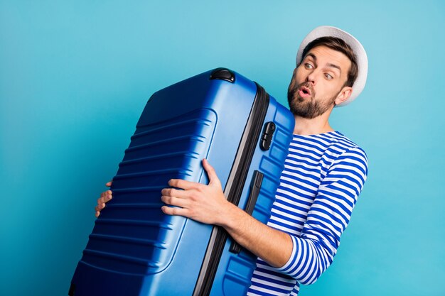 Foto di bel ragazzo viaggiatore tenere grande valigia volo aereo indennità di peso borsa troppo pesante sentire dolore alla schiena indossare camicia marinaio a strisce giubbotto panama isolato colore blu