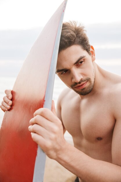 Photo of a handsome man surfer with surfing on a beach outside.