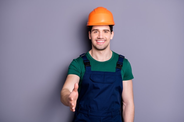 Photo of handsome masculine worker guy skilled engineer shaking arm boss customer making deal wear t-shirt blue safety dungarees protective helmet isolated grey wall