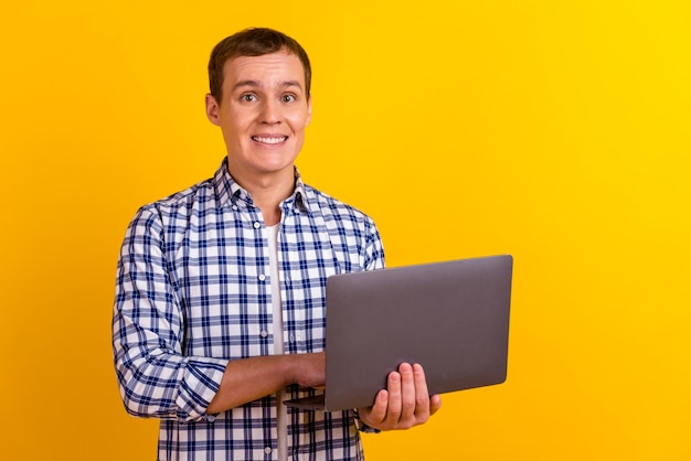 Photo of handsome satisfied young person hand hold netbook\
isolated on yellow bright color background