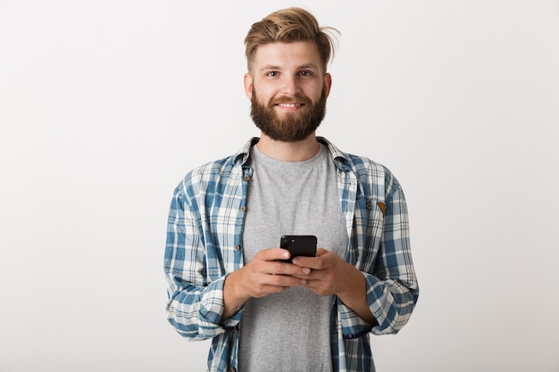 휴대 전화를 사용 하여 흰 벽 배경 위에 절연 서 잘 생긴 젊은 수염 된 남자의 사진.