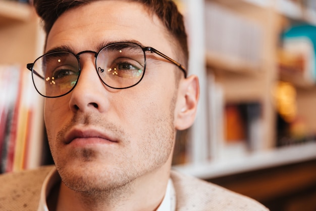 Photo of handsome young man wearing eyeglasses sitting in cafe and looking aside.