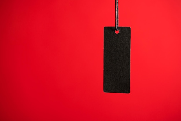 Photo of hanging black price tag on isolated red background with blank space