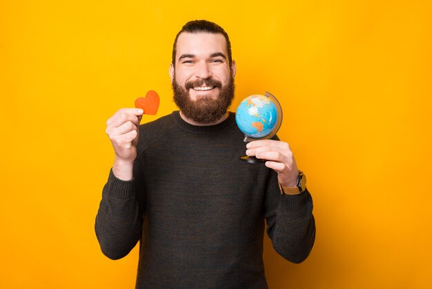 Photo of happy bearded handsome man holding globe and red heart