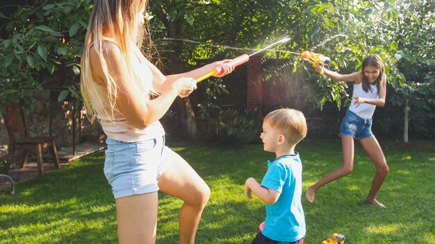 Photo of happy children having water gun fight at house backyard garden. Family playing and having fun outdoors at summer