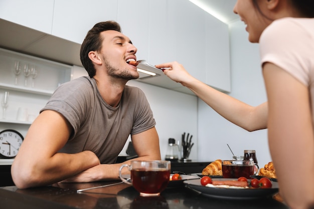 フラットでテーブルに座って、一緒に朝食を食べている幸せなカップルの男性と女性の写真