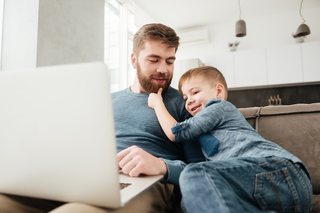 Photo of happy father using laptop computer with his little cute son.