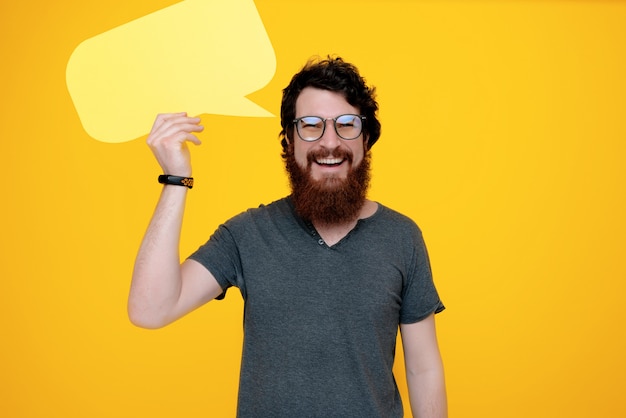 Photo of happy guy  wearing glasses, holding a bubble speech on yellow