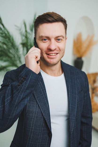 Photo of happy handsome man in classic jacket talking on mobile phone and smiling Remote work at home