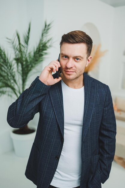 Photo of happy handsome man in classic jacket talking on mobile phone and smiling Remote work at home