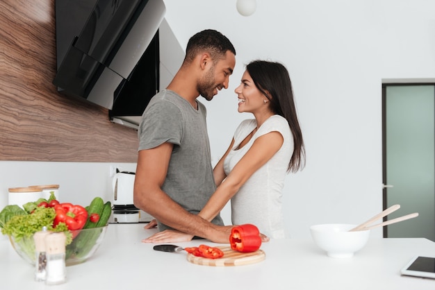 料理中に抱き締めるキッチンで幸せな愛情のあるカップルの写真。