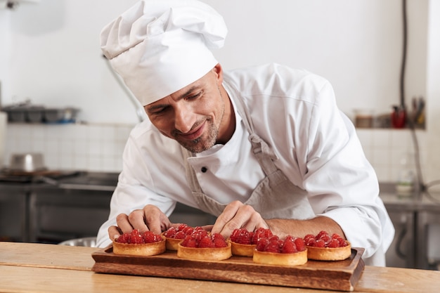 Foto del capo maschio felice in zolla bianca uniforme della tenuta con le torte