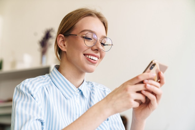 職場でドラフトを設計しながら携帯電話を使用して眼鏡で幸せな素敵な女性建築家の写真