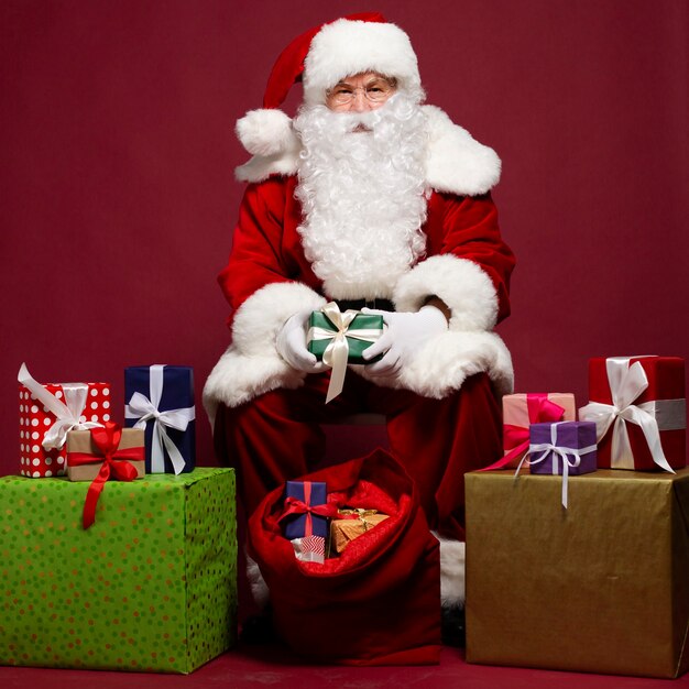 Photo of happy smiling Santa Claus with gifts boxes is posing 