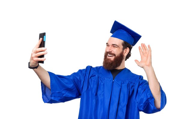 Photo of happy student man wearing blue robe and making selfie with smartphone