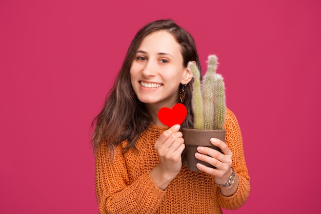 Photo of happy woman holding cactus plant and red heart shape