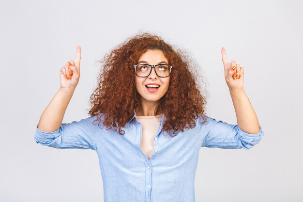 白い壁の背景の上に孤立して立っている幸せな若い巻き毛の女性の写真