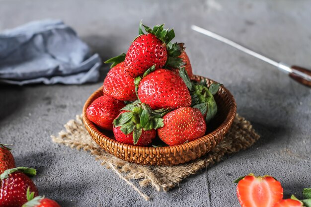 Photo of heap of fresh strawberries in the bowl on rustic grey background.
A bunch of ripe strawberries in a wooden bowl on the table. Copy space. Healthy fresh fruit. Organic food. Wooden basket