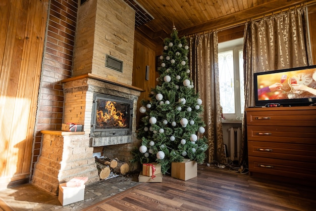 Photo of interior of room with a wooden wall, Christmas tree, fireplace. Christmas atmosphere. Home comfort