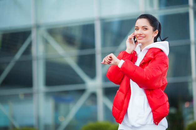 Фотография Joyful Fitness Woman 30s в спортивной одежде, касающейся наушника Bluetooth и держащего мобильный телефон во время отдыха в Грин-парке