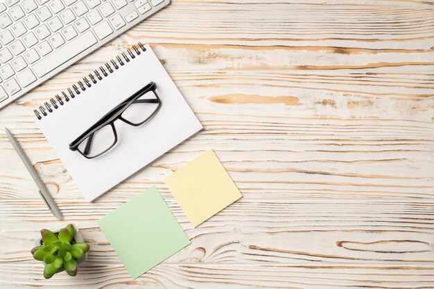 Photo above of keyboard plant glasses and notebook on the wood table