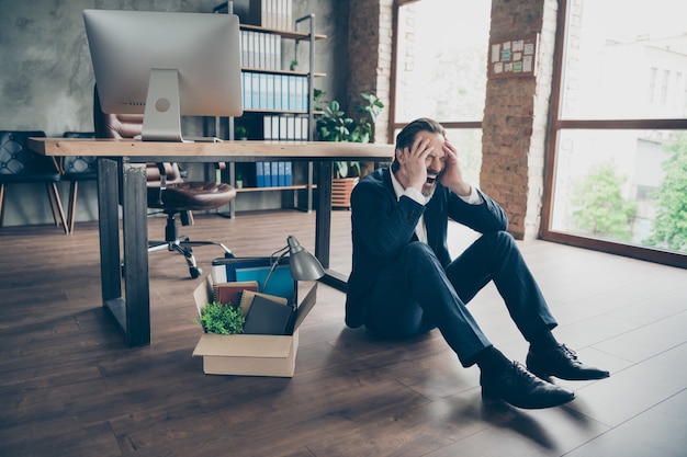 Photo of laid off dismissed sad worker mature guy fail fired agent lost job packed belongings box financial crisis sit floor wooden parquet hopeless cry yell workstation office indoors