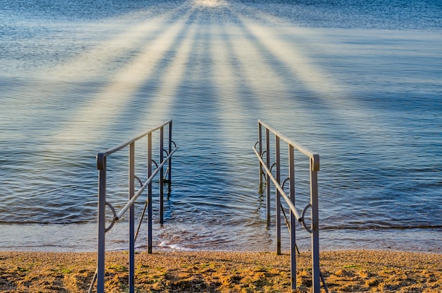 Foto una foto di un lago con una ringhiera metallica che fa filtrare i raggi del sole attraverso le nuvole.