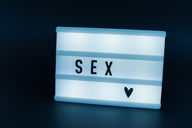 Photo of a light box with text, SEX, over isolated dark wall